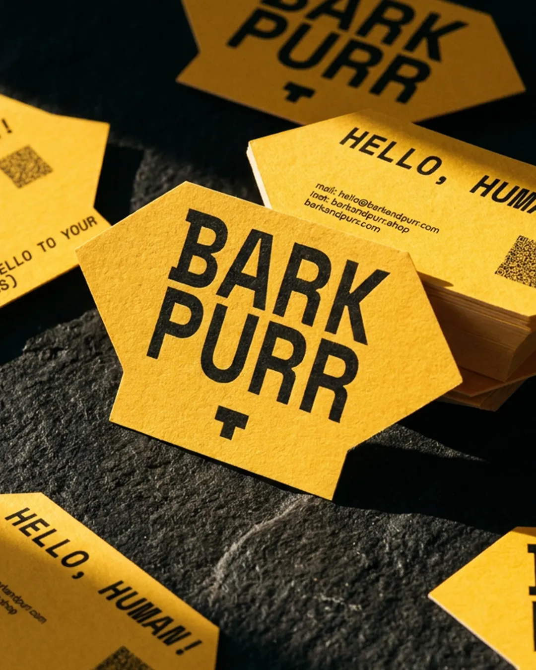 Yellow die-cut Bark & Purr business cards printed "Hello, human!" on dark stone