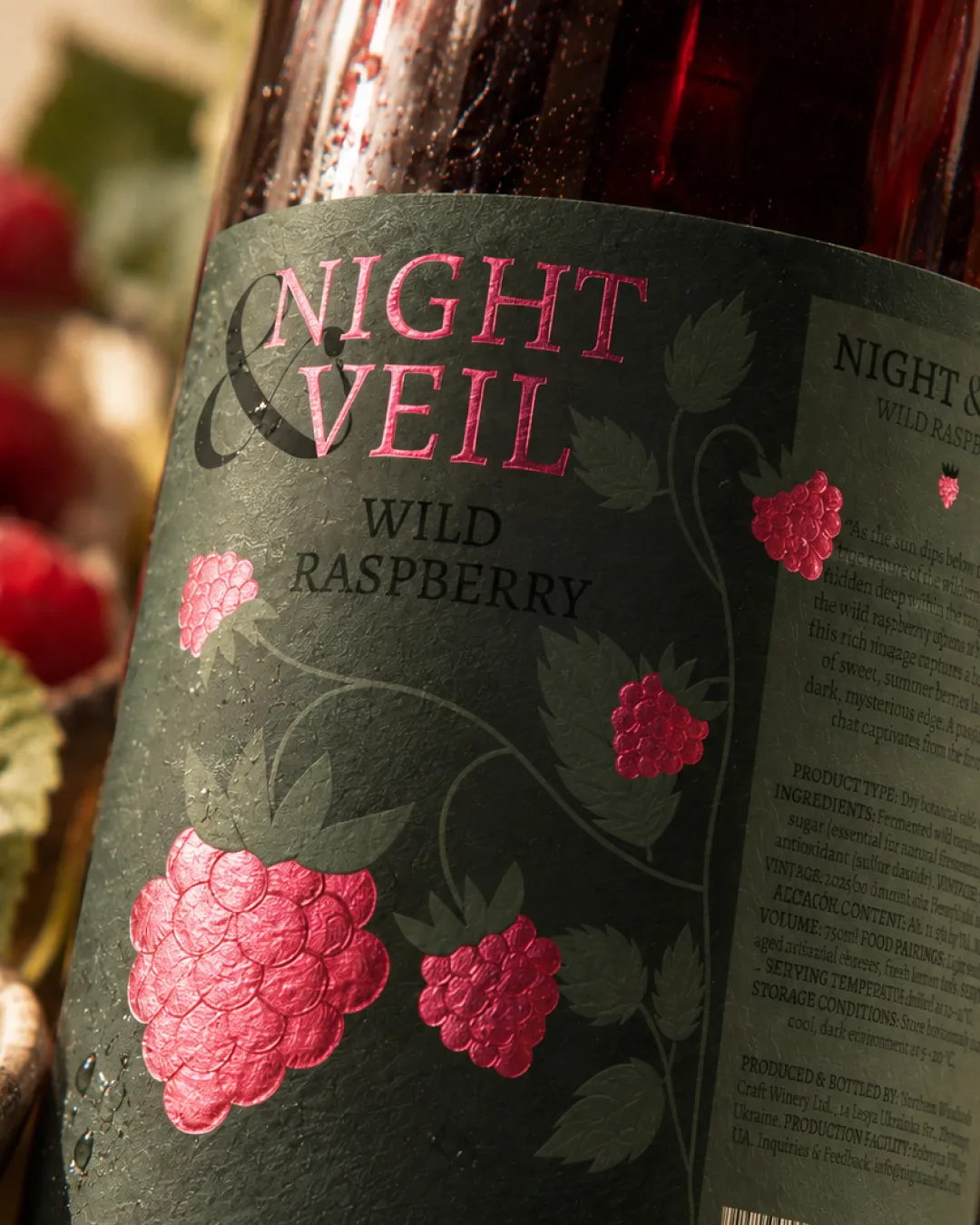 Close-up of the Night & Veil Wild Raspberry wine label with pink foil raspberries on textured dark green paper